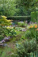 A pumped stream, edged with bog plants such as Hemerocallis - daylilies, Hosta and ferns
flows into a waterlily pond