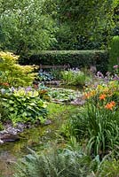 A pumped stream, edged with bog plants such as Hemerocallis - daylilies, Hosta and ferns tumbles down into
 a waterlily pond