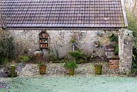 Terracotta pots, galvanised cans and baths and a shelf of decorative items are displayed against a barn. 
