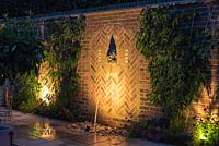 A small walled courtyard and seating area with illuminated water feature.