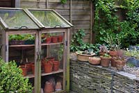 Small greenhouse with pots of succulents on stone gabion retaining wall