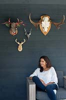 Woman sitting on outdoor garden chair with stag ornaments hanging on wall behind. 