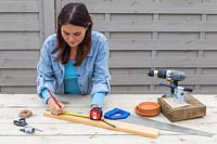 Woman using tape measure to mark along piece of wood.