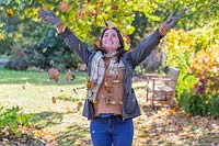 Woman throwing armful of autumnal leaves up into the air.