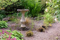 Birdbath in a gravel garden surrounded by self seeded Alchemilla mollis, linaria and  Geranium macrorrhizum at the Barn House, Glos in May