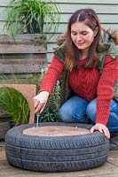 Woman using washers and bolts to secure wooden base onto tyre planter.