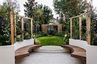 Contemporary garden with circular pergola area, with wooden seating. 