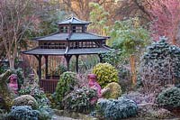 Japanese Tea House-style gazebo in frosted garden, with oriental statuary and shrubs and trees. 
