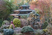Japanese Tea House-style gazebo in frosted garden, with oriental statuary and shrubs and trees.
