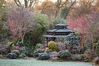 Japanese Tea House-style gazebo in frosted garden, with oriental statuary and shrubs and trees. The Four Seasons Garden, UK. 