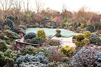Japanese Tea House-style gazebo in frosted garden, with oriental statuary and shrubs and trees. The Four Seasons Garden, UK.
