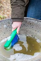 Close up of woman cleaning bird bath with scrubbing brush and soapy water. 