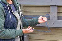 Woman pulling coated clothes hanger to shape it into a hook. 