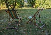 A pair of deck chairs on lawn with fallen leaves 