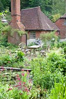 Rustic table and chairs on patio in informal cottage garden. Copyhold Hollow, Sussex, UK.