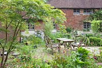 Rustic table and chairs on patio in informal cottage garden. Copyhold Hollow, Sussex, UK.