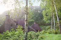 View of cottage surrounded by spring woodland garden. Copyhold Hollow, Sussex, UK. 