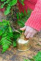 Using a hand-held metal mister on ferns in completed wreath