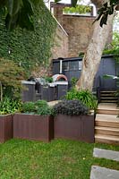 View of terrace patio in urban garden, with pizza oven and Cor-ten steel retaining wall turned planters. 
