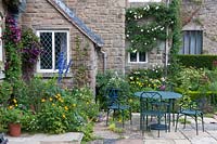Beds at base of house walls filled with flowering climbers such as 
Clematis 'Warszawska Nike' and Clematis 'Etoile Violette', nearby a paved courtyard area with table and
 chairs