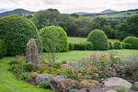 Rock garden with shrub and ground cover roses, with view over hills.