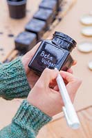 Woman writing with chalk marker pen onto painted glass jar.