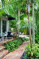 View of patio and terrace with table and chairs surrounded by Solitaire palms. Key West Classic Garden, designed by Craig Reynolds. Key West, Florida, USA.
