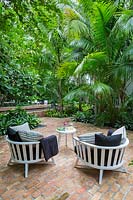 Two low wooden garden chairs in tropical garden. Key West Classic Garden, designed by Craig Reynolds. Key West, Florida, USA.
