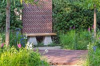 View across path and flower beds of the 'South Oxfordshire Landscape Garden' to
 the bench topped with Scottish oak with staddle stones and brick screen between hedges 


