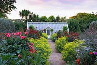 A brick path, leading through a restored Victorian walled kitchen garden to a greenhouse, is edged with clumps of Euphorbia ceratocarpa, interspersed with dahlias, asters, Verbena bonariensis and clipped bay trees.
