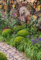 Topiary balls surrounded by ornamental grasses, backed by beech log wall. The Very Hungry Caterpillar Garden, RHS Tatton Park Flower Show, 2019.
