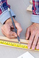 Woman measuring length of wooden strips with tape measure. 