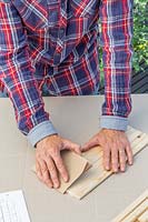 Woman smoothing the ends of freshly cut wood using sandpaper. 