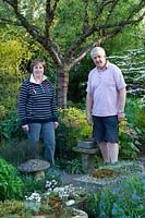 Couple in their garden with pots of alpines and rockery plants. 
