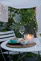 A secluded dining area in the garden made by draping a sheet between rope supports and hanging fairy lights around the edge of the sheeting