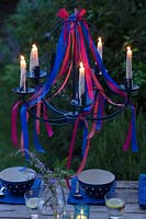 The beautiful ribbon chandelier over a dining table at dusk with all the candles lit. 