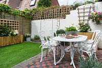 Tiny courtyard garden with tiled area, metal furniture, raised beds and artificial grass