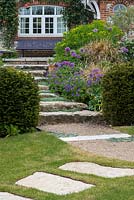 Stepping stones in a lawn lead to stone steps, interspersed with woolly thyme, and edged in Geranium x magnificum 'Rosemoor' and Allium 'Purple Sensation',