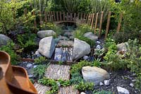 Through Your Eyes Garden. Wooden seating area with slate pieces inlaid into corten steel frames to form stepping stones. Water pool with 'split' rock.   Planting includes Deschampsia cespitosa, Achillea 'Moonshine', Ophiopogon planiscapus 'Nigrescens' - Sponsors: Kebony, CED Stone, R and G Metal Products, William's Art and Design, Practicality Brown.
