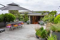 London roof terrace with wood decking and contemporary grey chairs, table and parasol. With large raised containers with perennials and annuals forming a natural screen for privacy. Flowers include  Verbena bonariensis, Lavandula angustifolia Hidcote, Juncus maritimus.