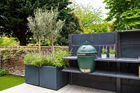 Modern outdoor kitchen with BBQ and containers with Olea europaea 'Olive trees' and Salvia officinalis.