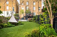 View across the garden with artificial grass and cacoon hanging tent towards the house,  outdoor kitchen and dining area.  