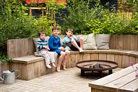 Children seating on the bench by fire pit in the garden.