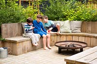 Children sitting on the bench by fire pit in the garden.