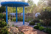 A garden designed to show how to cope with climate change. A rainfall pavilion with rain chains channelling water into the garden. Large natural stones form a contemporary rock garden, with drought tolerant plants including Pinus mugo, Lychnis coronaria 'Alba', at the RHS Hampton Court Palace Garden Festival 2019. Sponsor: Thames Water