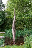 Bronze shard by David Harber set in a pool surrounded by Iris pseudacorus - The Savills and David Harber Garden, RHS Chelsea Flower Show 2019.