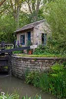 Lock keeper's office next to the lock gates with herbaceous planting of Lupins and Delphiniums - The Welcome to Yorkshire Garden, RHS Chelsea Flower Show 2019