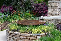 Dry stone wall raised bed with circular pool, underplanted with Carex, Erigeron karvinskianus and Ajuga reptans, Geum in background -  Miles Stone: The Kingston Maurward Garden, RHS Chelsea Flower Show 2019