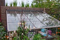 Sunken lean-to greenhouse next to a gabion wall - The Montessori Centenary Children's Garden, RHS Chelsea Flower Show 2019