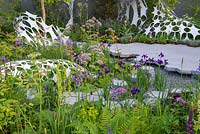 Hexagonal paving next to a pond with Iris sibirica 'Caesar's Brother', ferns and sculpture by Liam Hopkins - The Manchester Garden, RHS Chelsea Flower Show 2019.